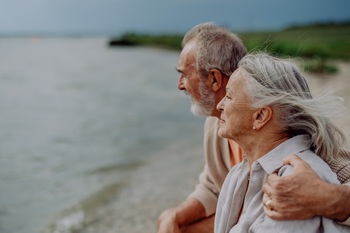 Older couple on the shoreline of a body of water.  