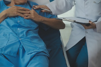 Hospitalized man lying in bed while doctor checking his pulse. Female physician examining male patient in hospital room.